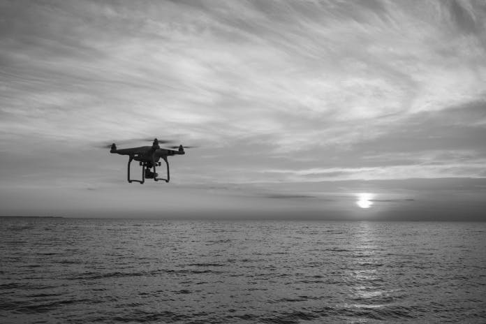 a remote controlled flying over the ocean at sunset